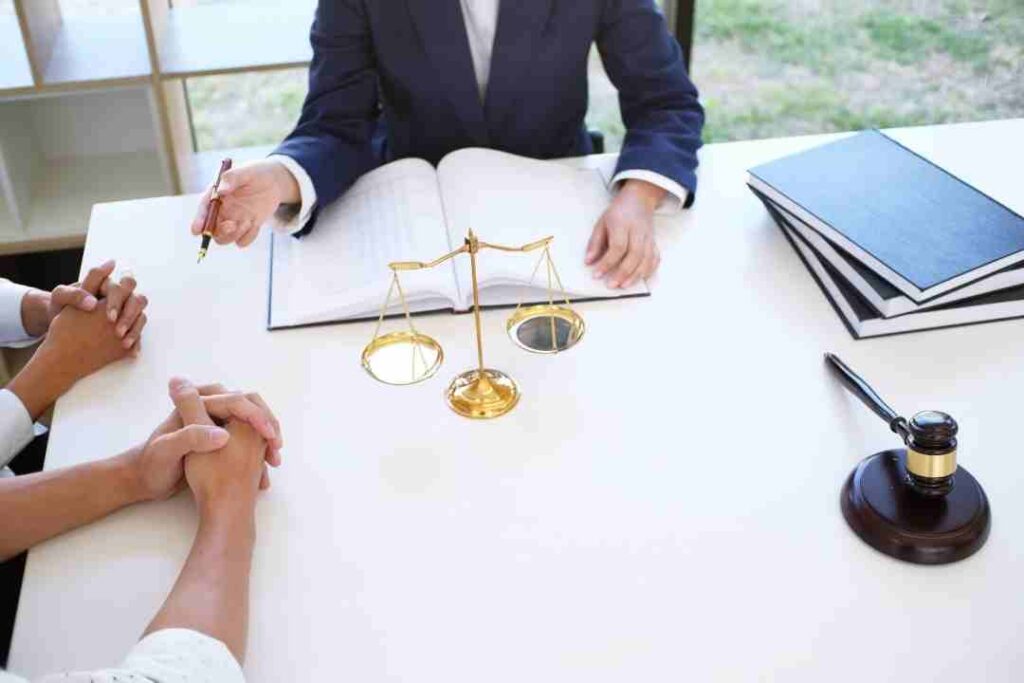 Lawyer consulting with clients at a desk with an open book, scales, and a gavel.