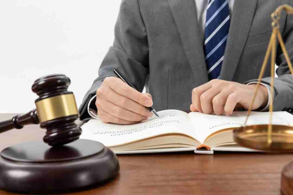 Lawyer writing in an open law book next to a gavel and scales.